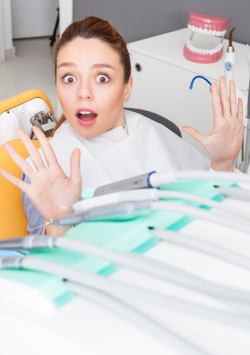 Portrait of a young woman is scared at dentist visit. She is rejecting examining  with her hands up.