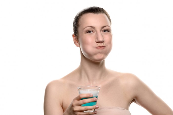 Healthy happy woman rinsing and gargling while using mouthwash from a glass, during daily oral hygiene routine, portrait with bare shoulders, with copy space, isolated on white