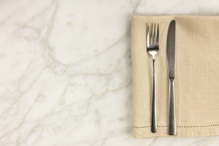 An overhead photo of a retro fork and knife on a white marble table. A restaurant menu or special offer banner design template